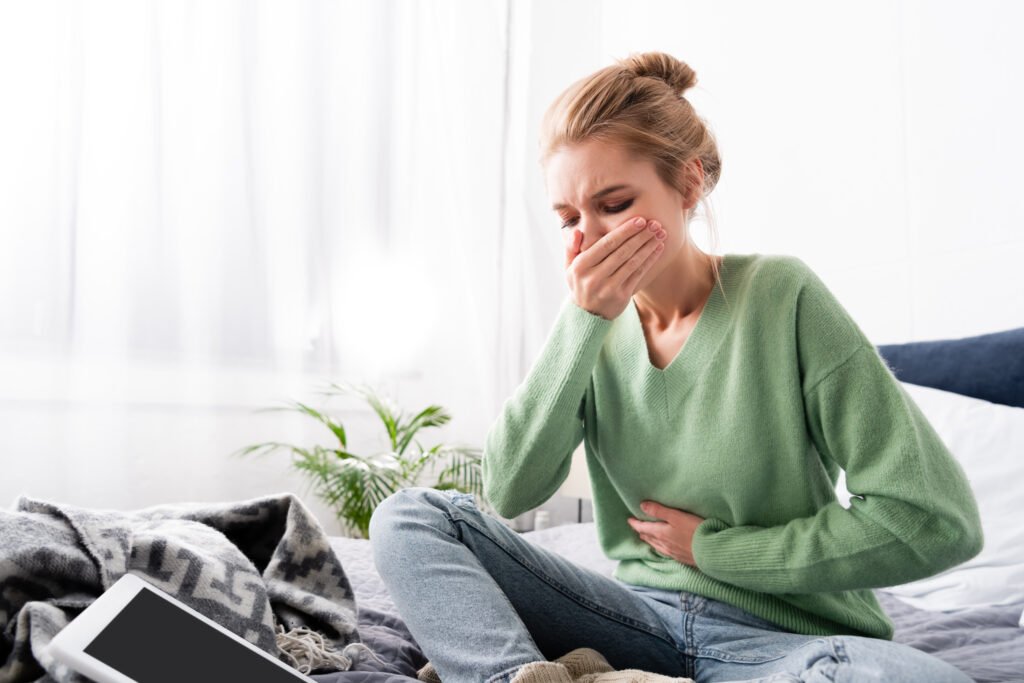 woman having nausea and sitting on bed with digital device