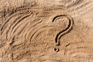 question marks written on beach sand close up, with copy space.