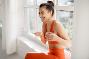 Happy woman takes supplements or vitamins in the form of capsules after training in the gym. Concept of additional nutrition during training